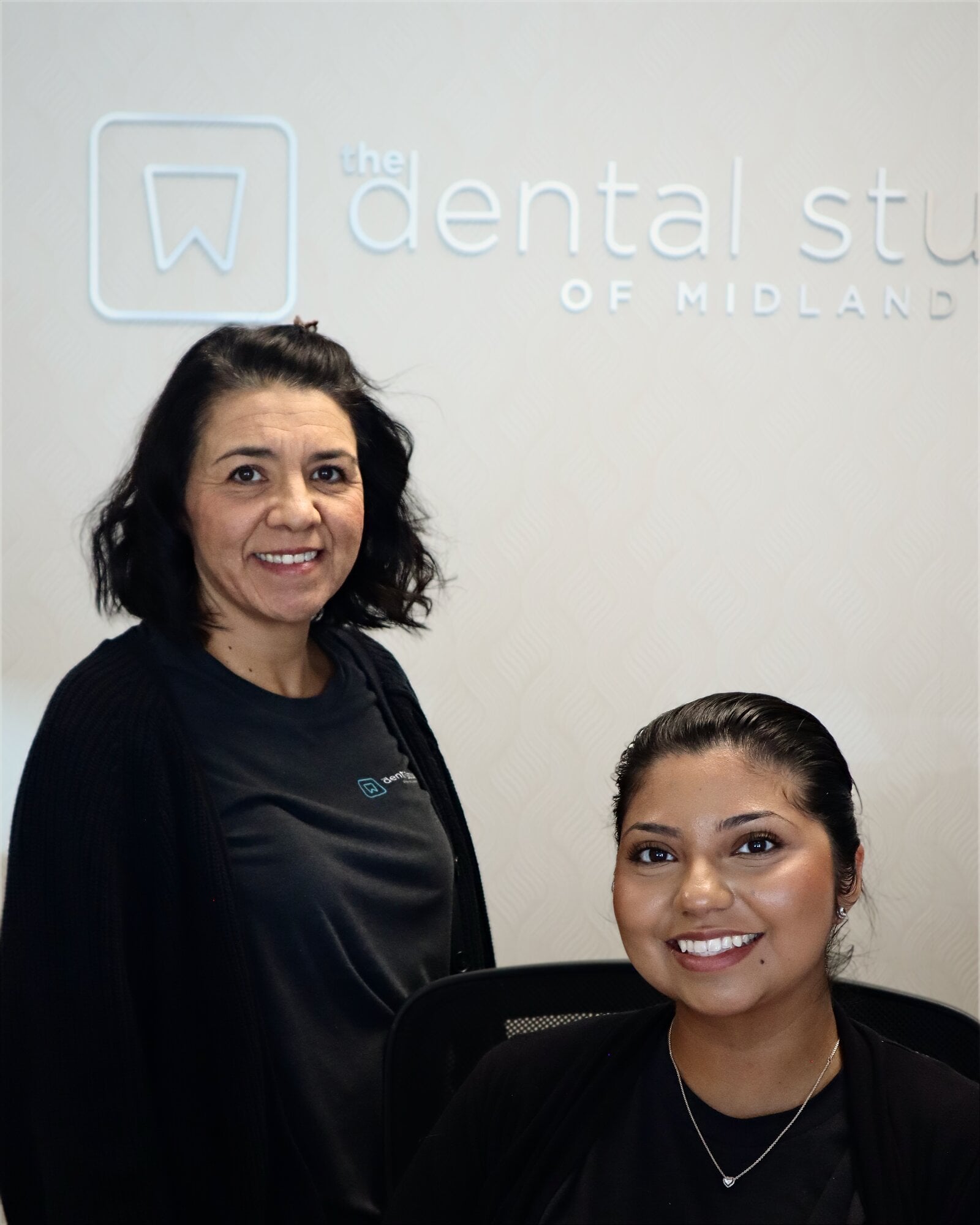 Two front desk team members smiling under The Dental Studio of Midland logo