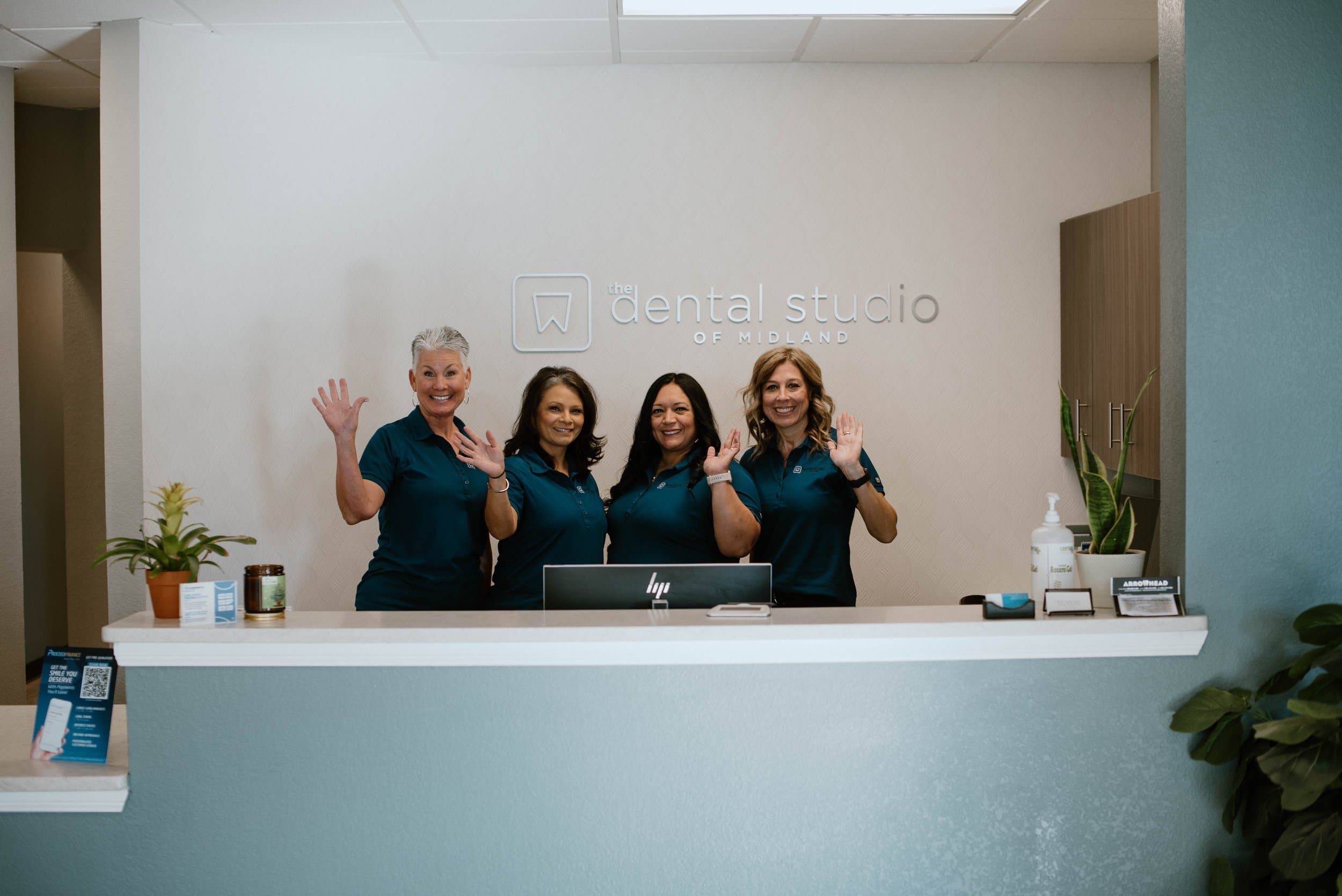 The front desk team waving from the reception desk at The Dental Studio of Midland