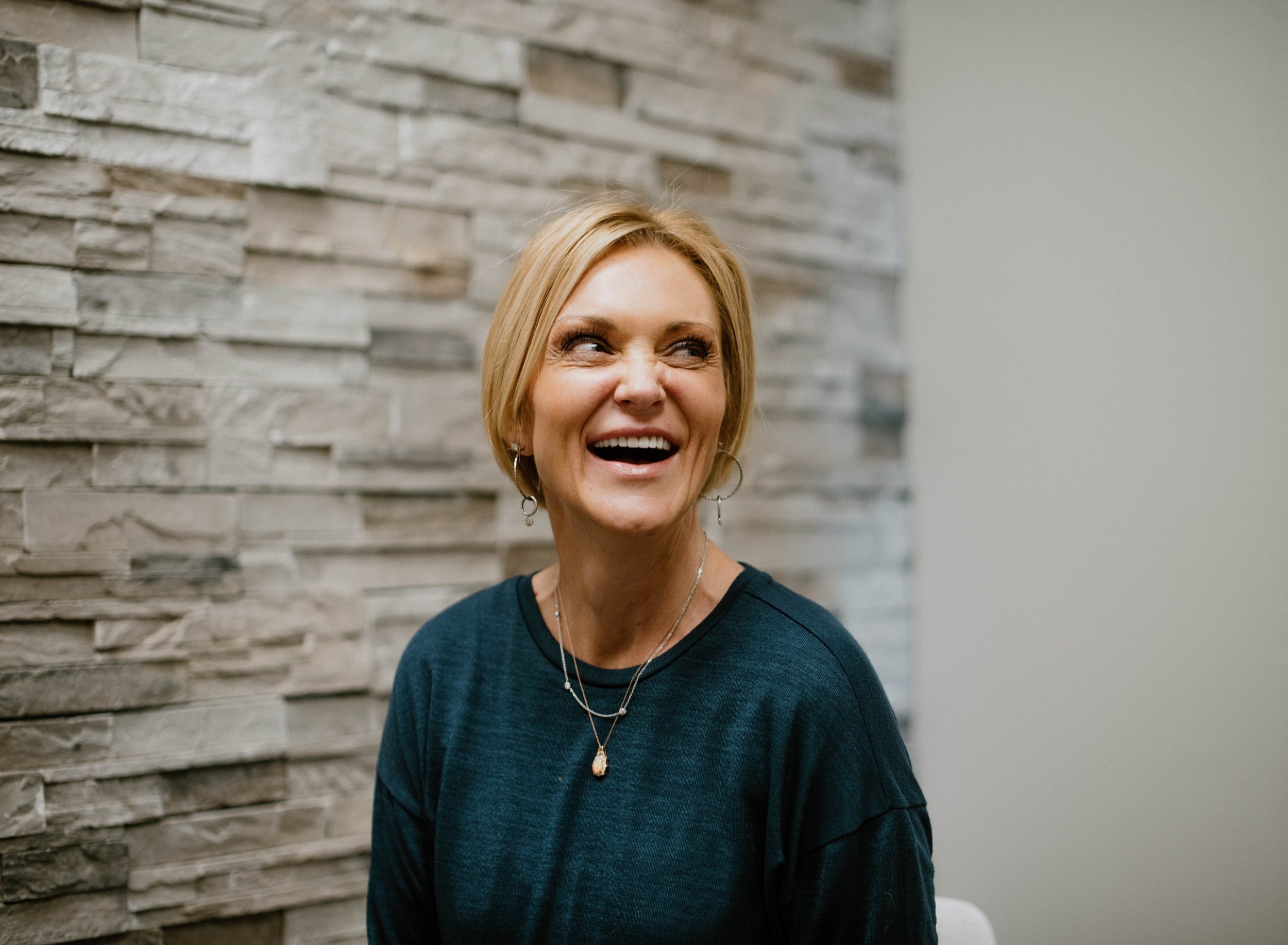 A patient laughing in front of the stone accent wall at The Dental Studio of Midland